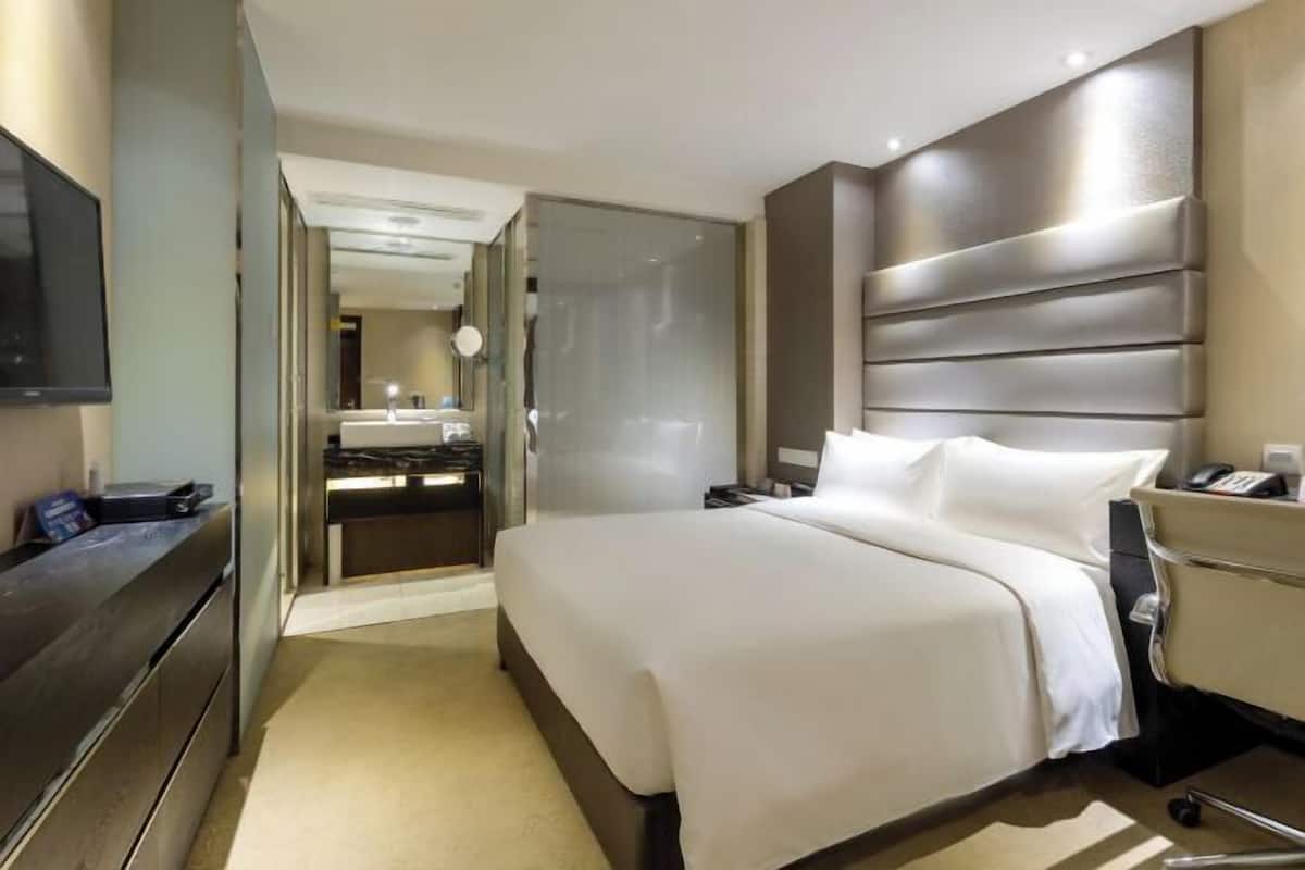Une chambre d’hôtel comprenant un lit, une table de chevet, une télévision et une salle de bain avec un lavabo et un miroir.