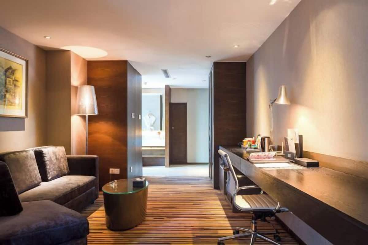Une chambre d’hôtel moderne, équipée d’un canapé, d’un bureau avec une lampe, d’une table basse et offrant une vue sur le couloir.