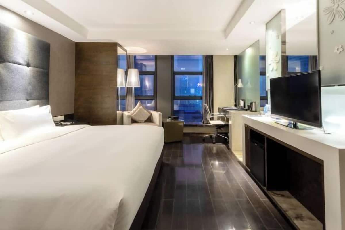 Une chambre d’hôtel avec un grand lit, un bureau, une télévision et une vue sur la ville par la fenêtre.