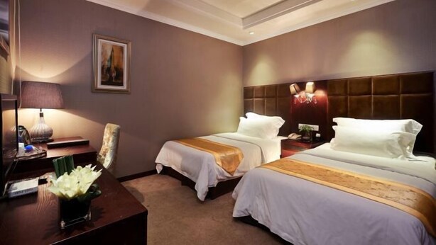 A hotel room with two beds, a desk, a lamp, a painting, and a nightstand with a phone and a plant. - Chongqing Huangqiao Hotel (Three Gorges Museum Children's Hospital) (Chongqing)