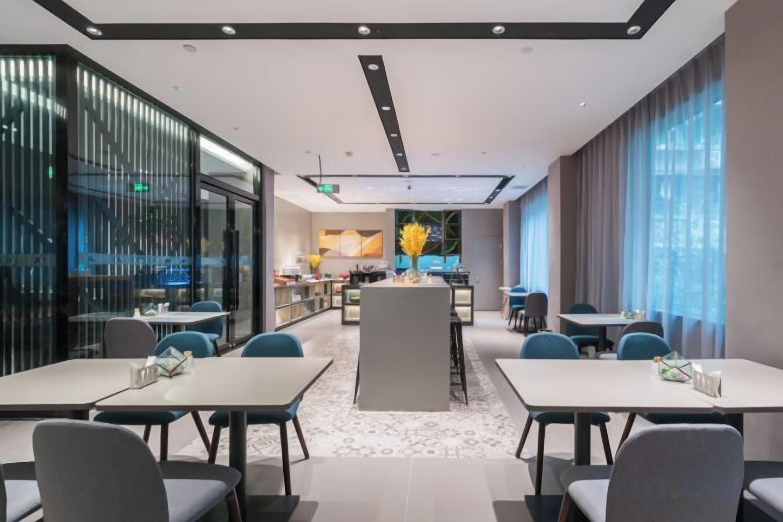 A modern hotel lobby with a central island, seating arrangements, and a view of the kitchen area.