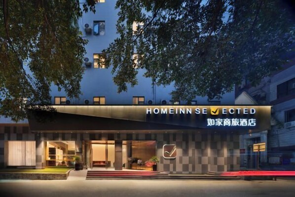 A hotel entrance with a checkmark sign, a modern facade, and a well-lit entrance area.