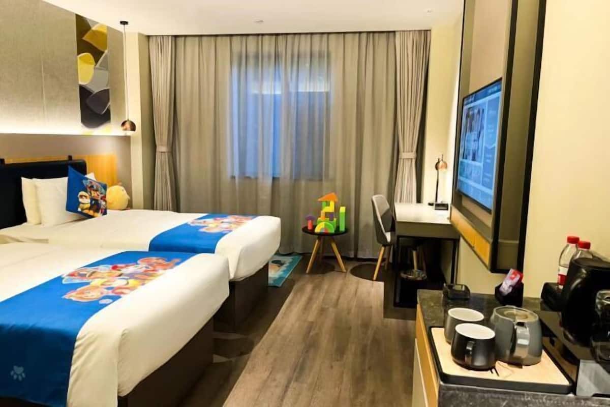 A hotel room with two beds, a desk, a chair, a TV, and a coffee station.