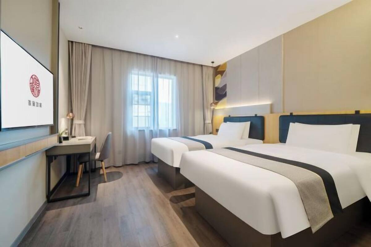 A hotel room with two beds, a desk, and a large window with curtains.