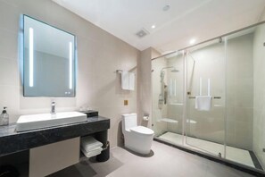 A modern bathroom with a large mirror, a sink, a toilet, and a glass-enclosed shower area.