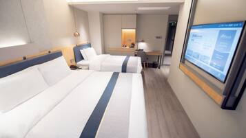 A hotel room with two beds, a desk, a chair, a TV, and a bathroom.