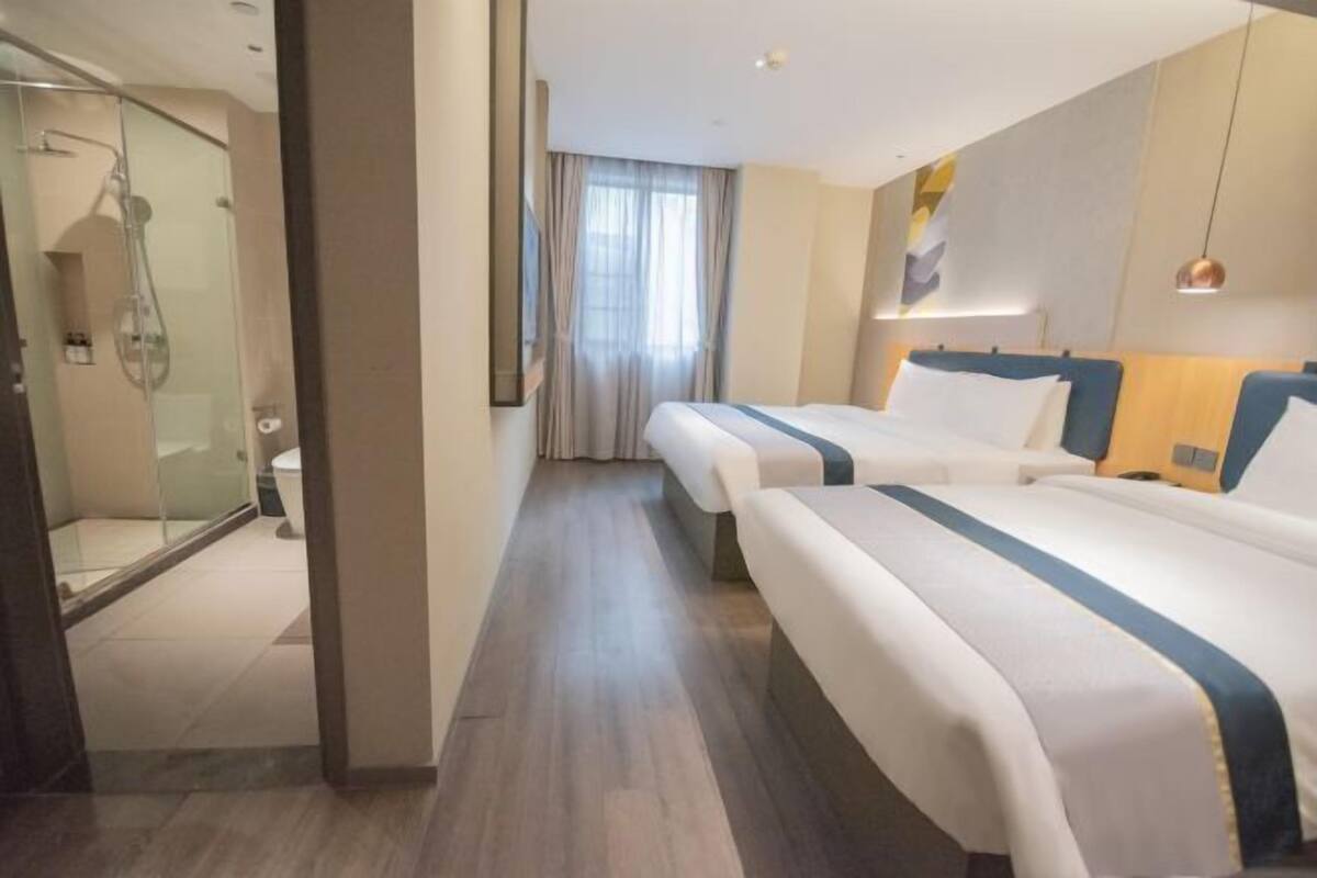 A hotel room with two beds, a shower, and a large window with curtains.