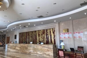 Zona de recepción de un hotel con un mostrador de mármol, una pared con diplomas enmarcados y un techo curvo con iluminación empotrada.