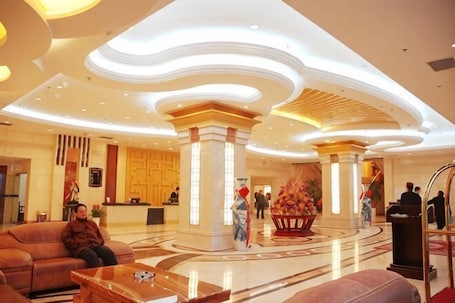 A hotel lobby with a reception desk, seating area, and decorative columns.. Zhulinshan Hotel
