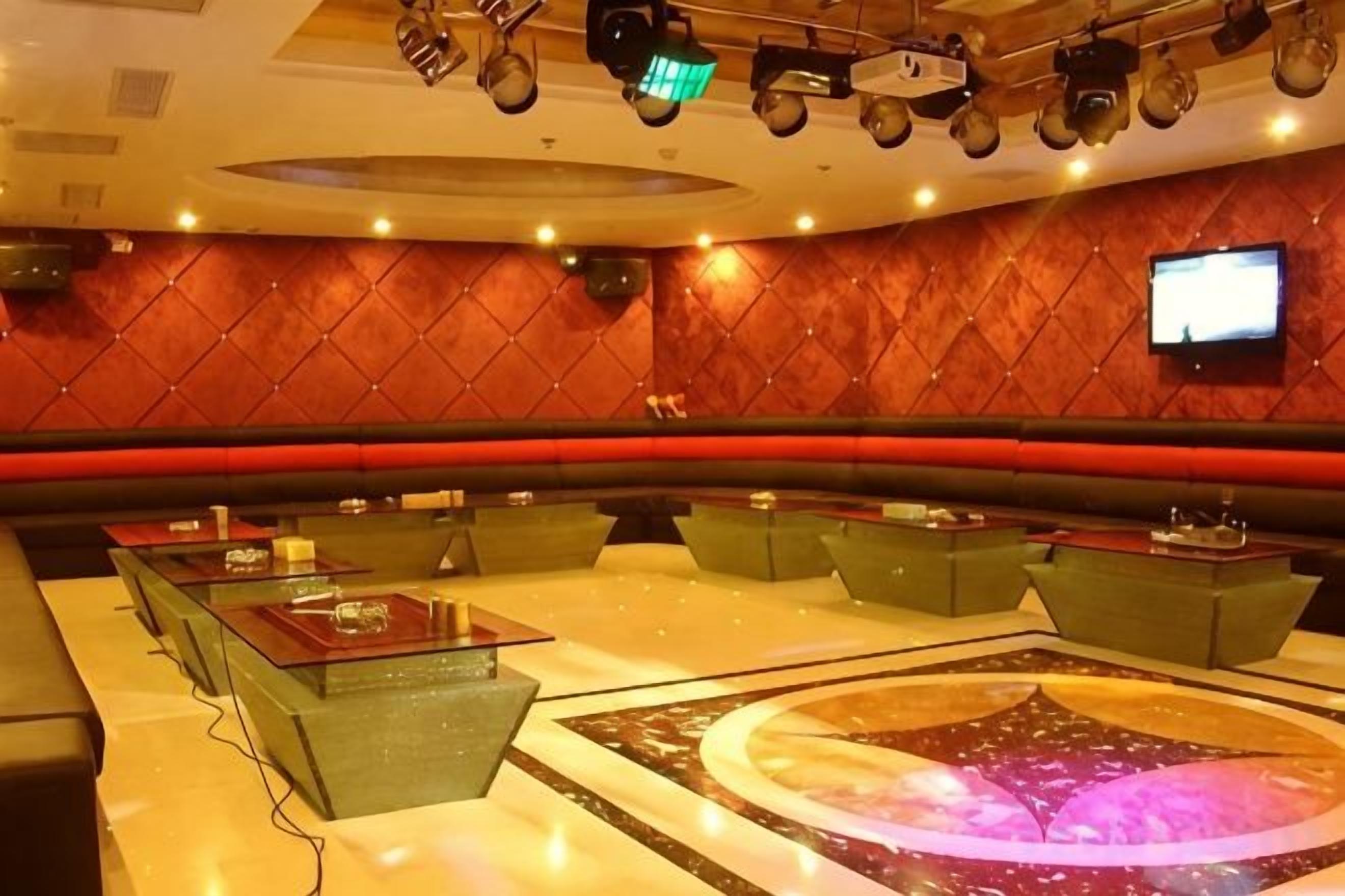 A hotel lobby with a curved seating area, a central table with a projection, and a television on the wall.