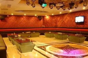 A hotel lobby with a curved seating area, a central table with a projection, and a television on the wall.