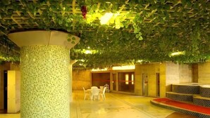 Un hall d’entrée avec une colonne à motifs verts, un espace détente avec des chaises blanches et une moquette rouge.