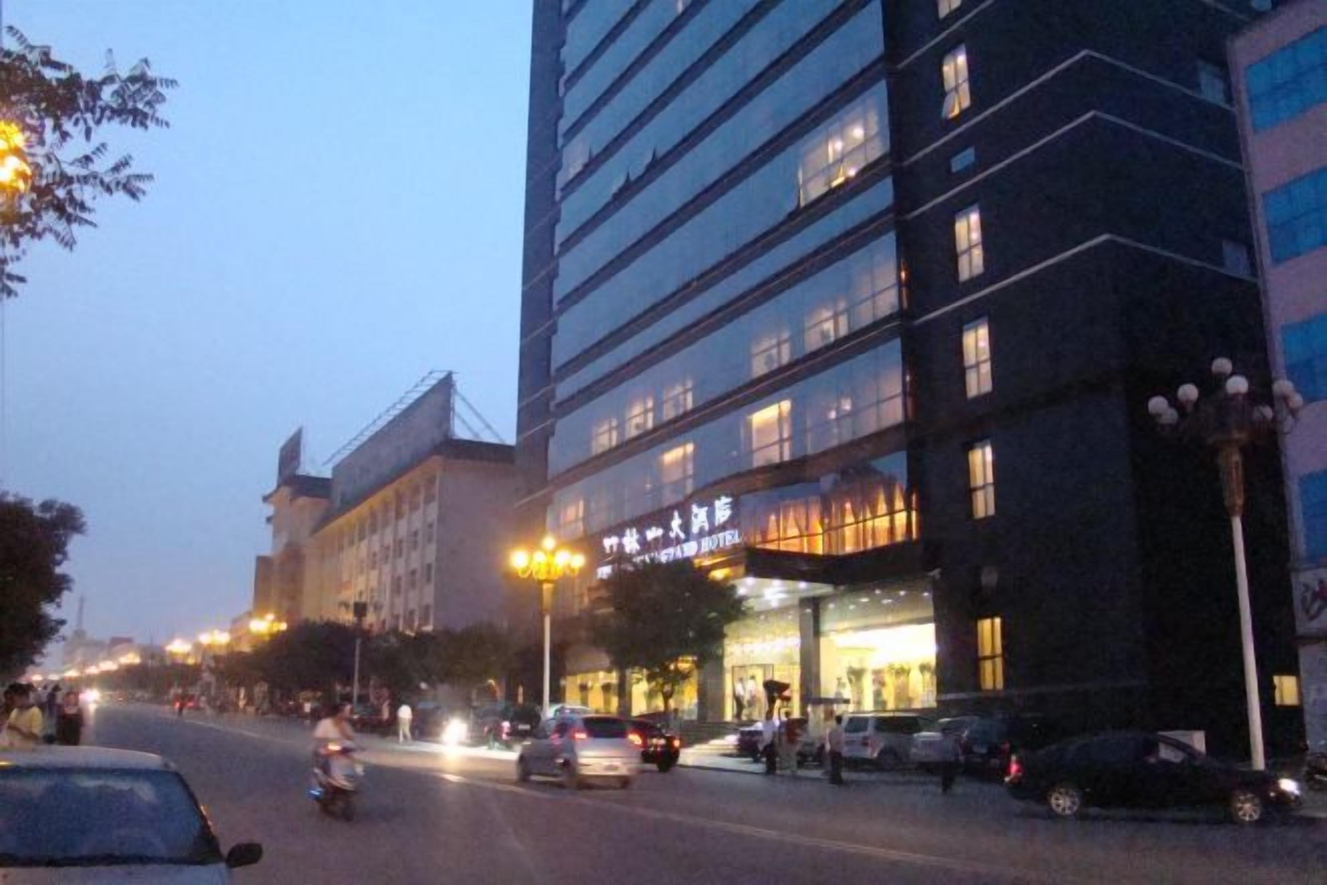 Ett hotell med flera våningar, upplyst skyltning, en gata framför och parkerade bilar.