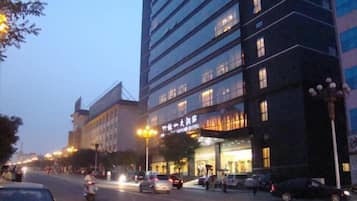 Ett hotell med flera våningar, upplyst skyltning, en gata framför och parkerade bilar.
