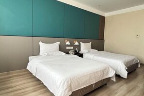 Habitación de hotel con dos camas, una pared de acento color turquesa y piso de madera.