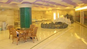 Un hall d’entrée avec une table ronde et des chaises, un pilier vert et un mur décoratif orné d’un motif ondulé.