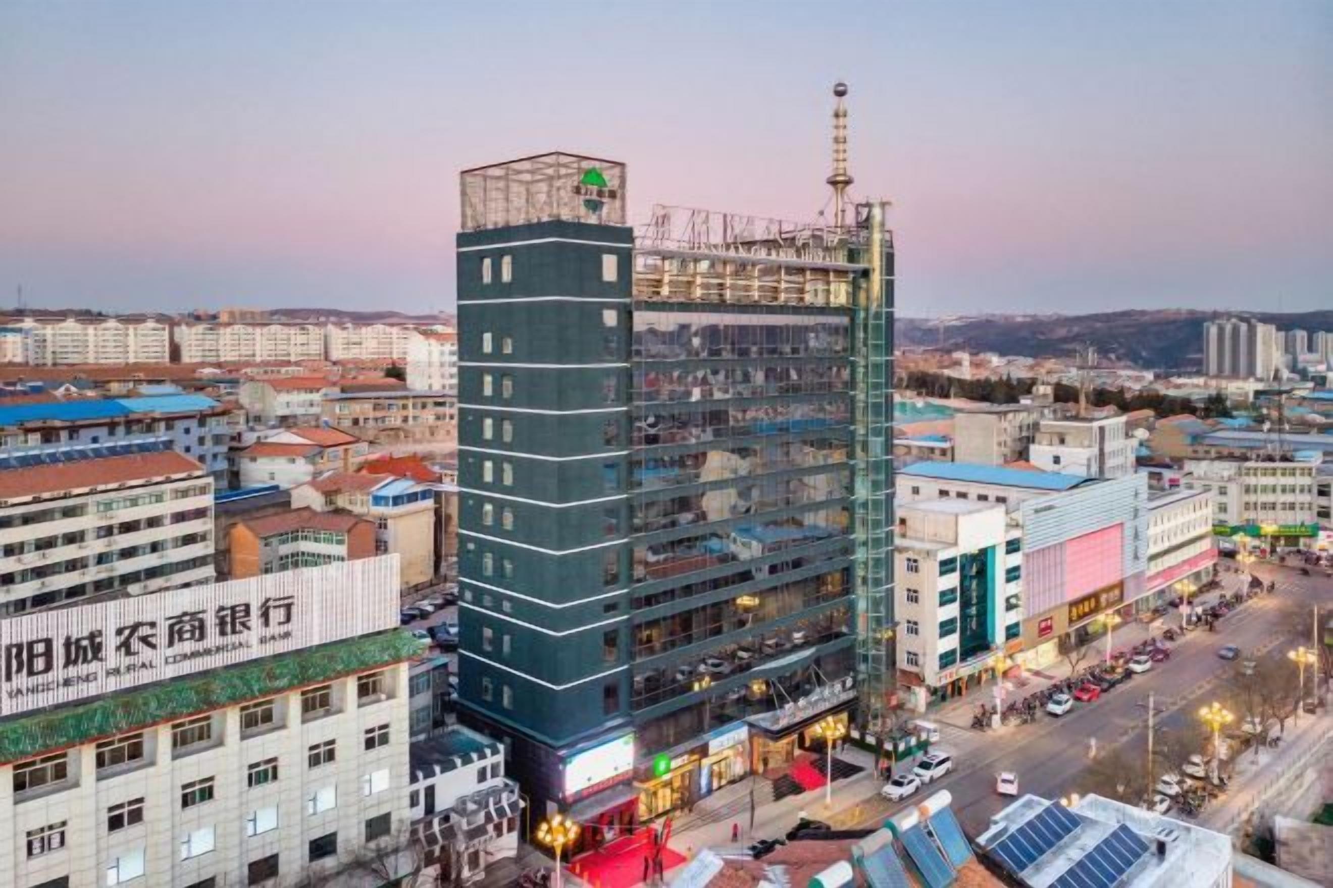 A multi-story building with a prominent antenna on top, surrounded by other buildings and a busy street.