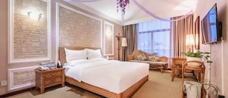 Quarto de hotel com uma cama grande, área de estar com sofá e televisão na parede.