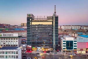 Un edificio de varios pisos con una aguja destacada, rodeado de otros edificios y una concurrida calle.