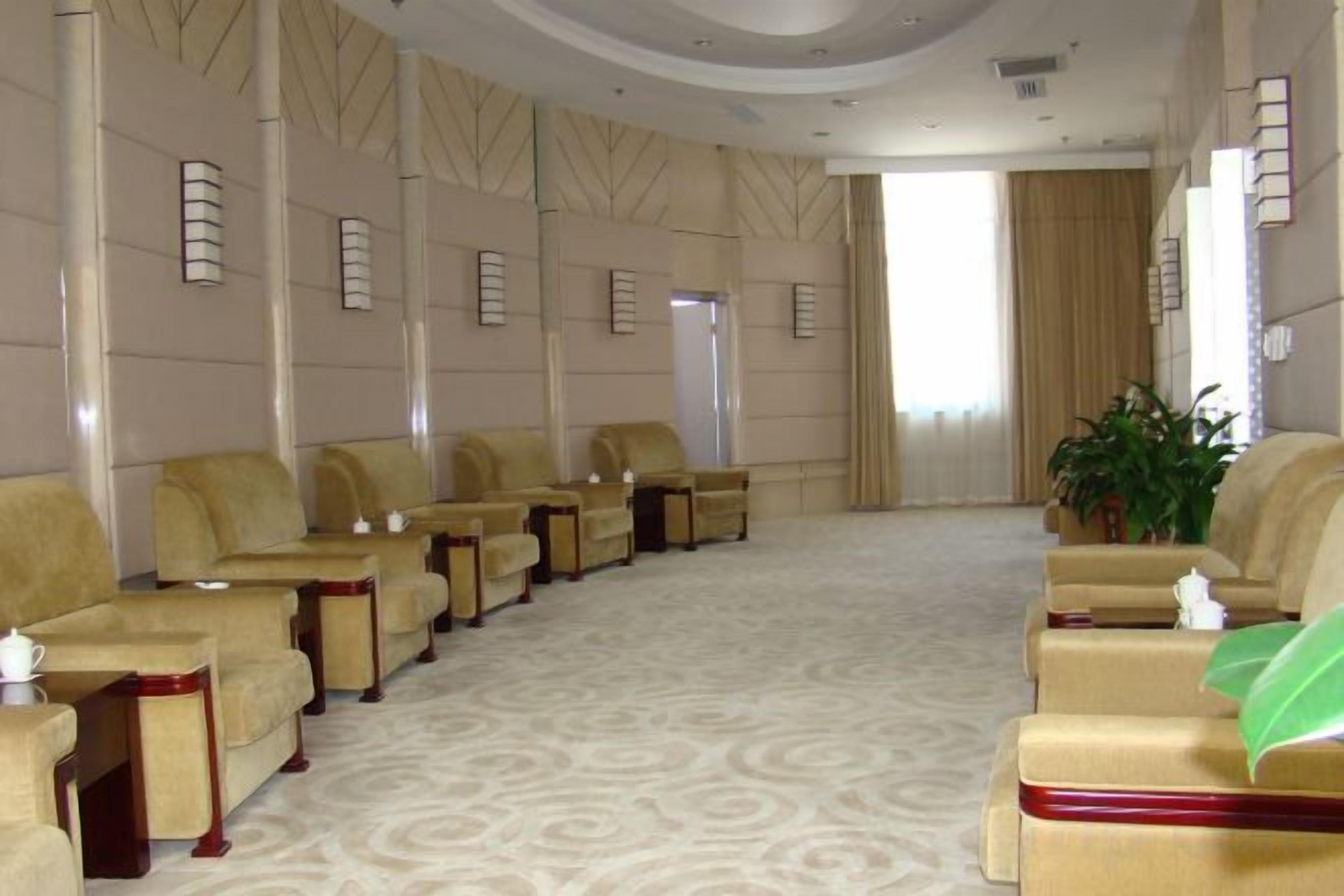A hotel room with a row of beige sofas, a carpeted floor, and a large window with curtains.