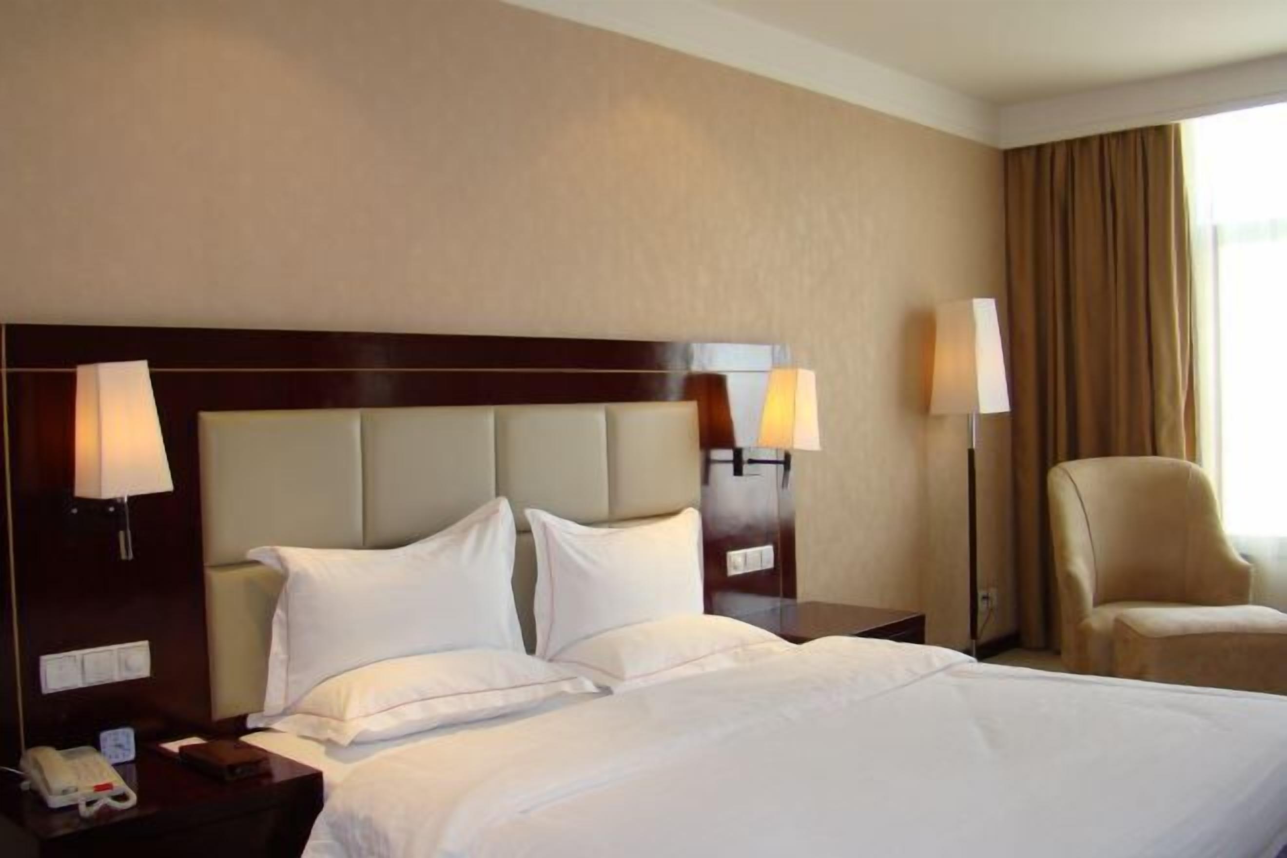 Une chambre d’hôtel avec un grand lit, deux lampes de chevet, une chaise et une table de chevet avec un téléphone et une lampe.