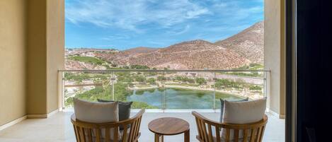 A balcony with two wooden chairs and a small table, overlooking a river and mountains.
