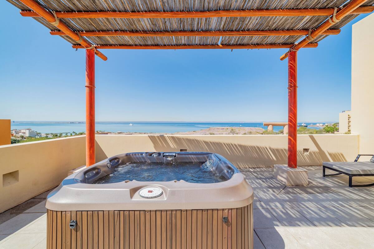 A hot tub under a wooden pergola with a view of the sea.
