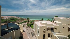A coastal hotel with a pool, palm trees, and a view of the sea.