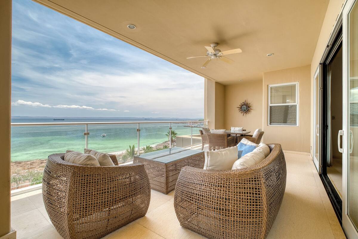 A balcony with wicker furniture, a ceiling fan, and a view of the ocean.