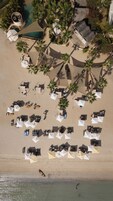Vista aérea de una playa con múltiples tumbonas y sombrillas, palmeras y una piscina.