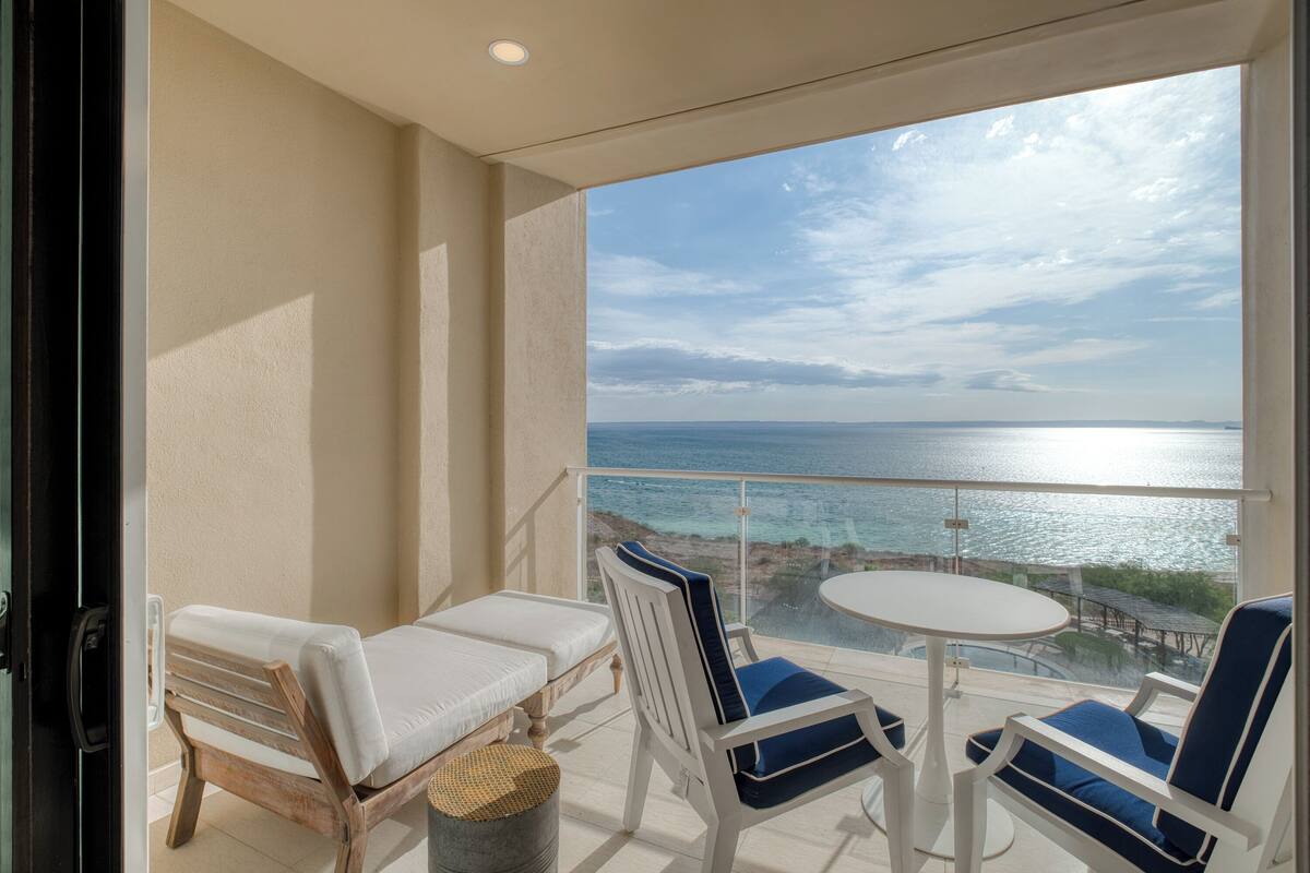 A balcony with a view of the sea, two lounge chairs, a small table, and a wicker basket.