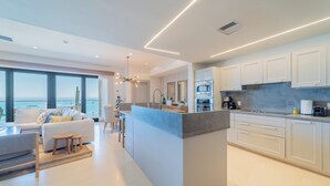 Una cocina moderna con armarios blancos, una isla central y vistas al océano.