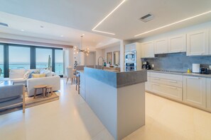 A modern kitchen with white cabinets, a central island, and a view of the ocean. - Puerta Cortés Residences by Lumina (La Paz)