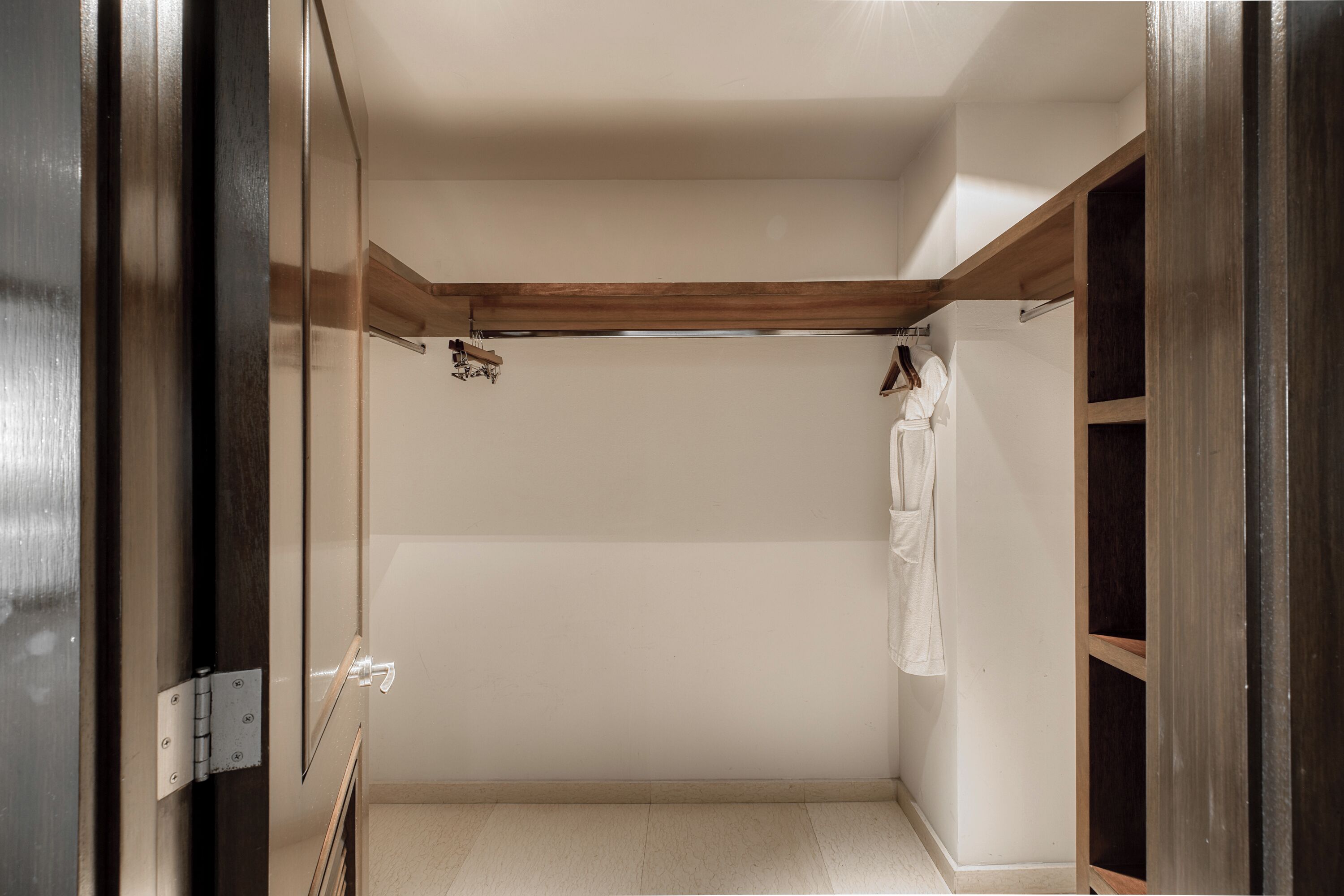 A walk-in closet with a wooden beam ceiling, a hanging rod, and a white towel on the right.