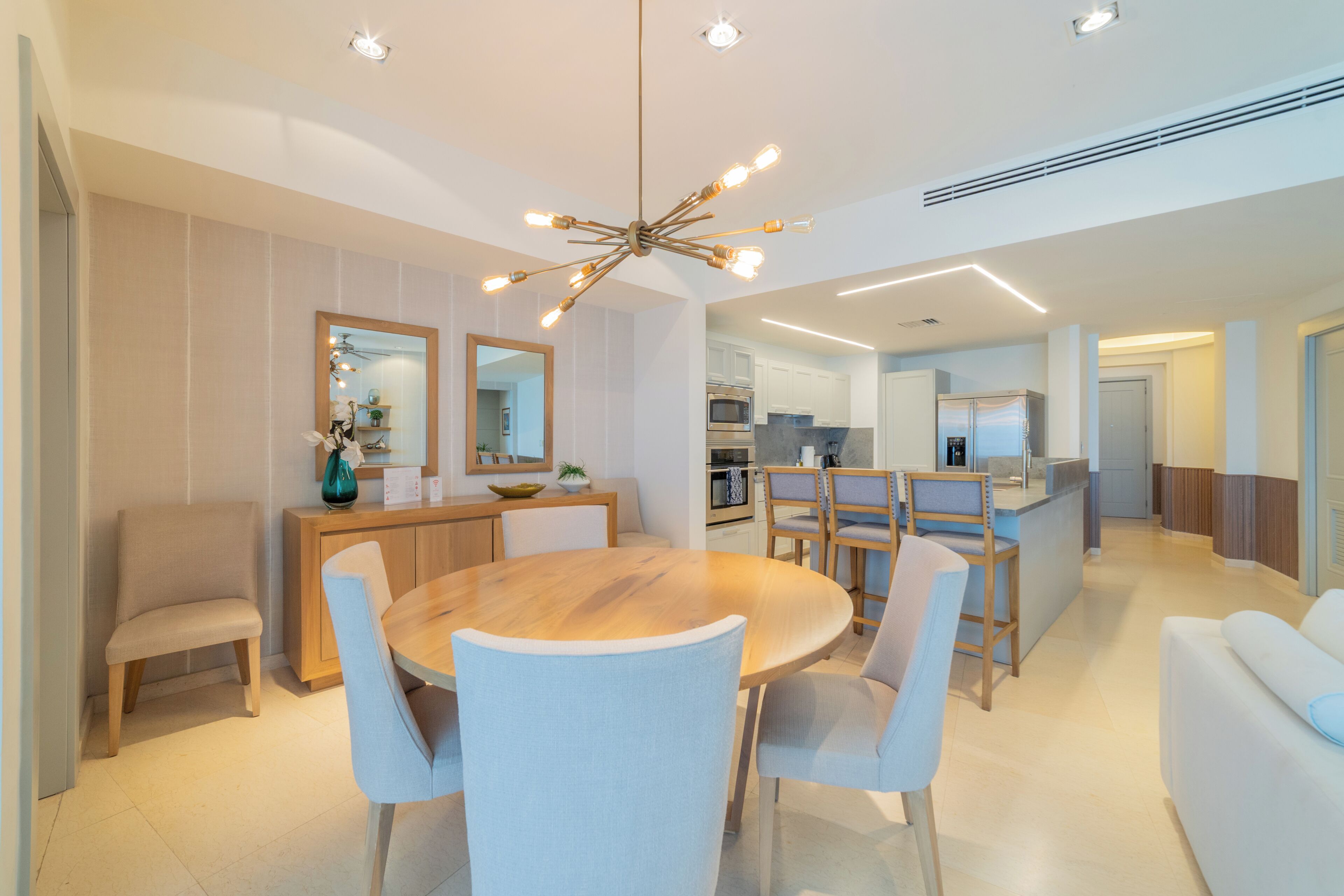 A modern kitchen with a central island, a dining area with a round table and chairs, and a living area with a sofa.