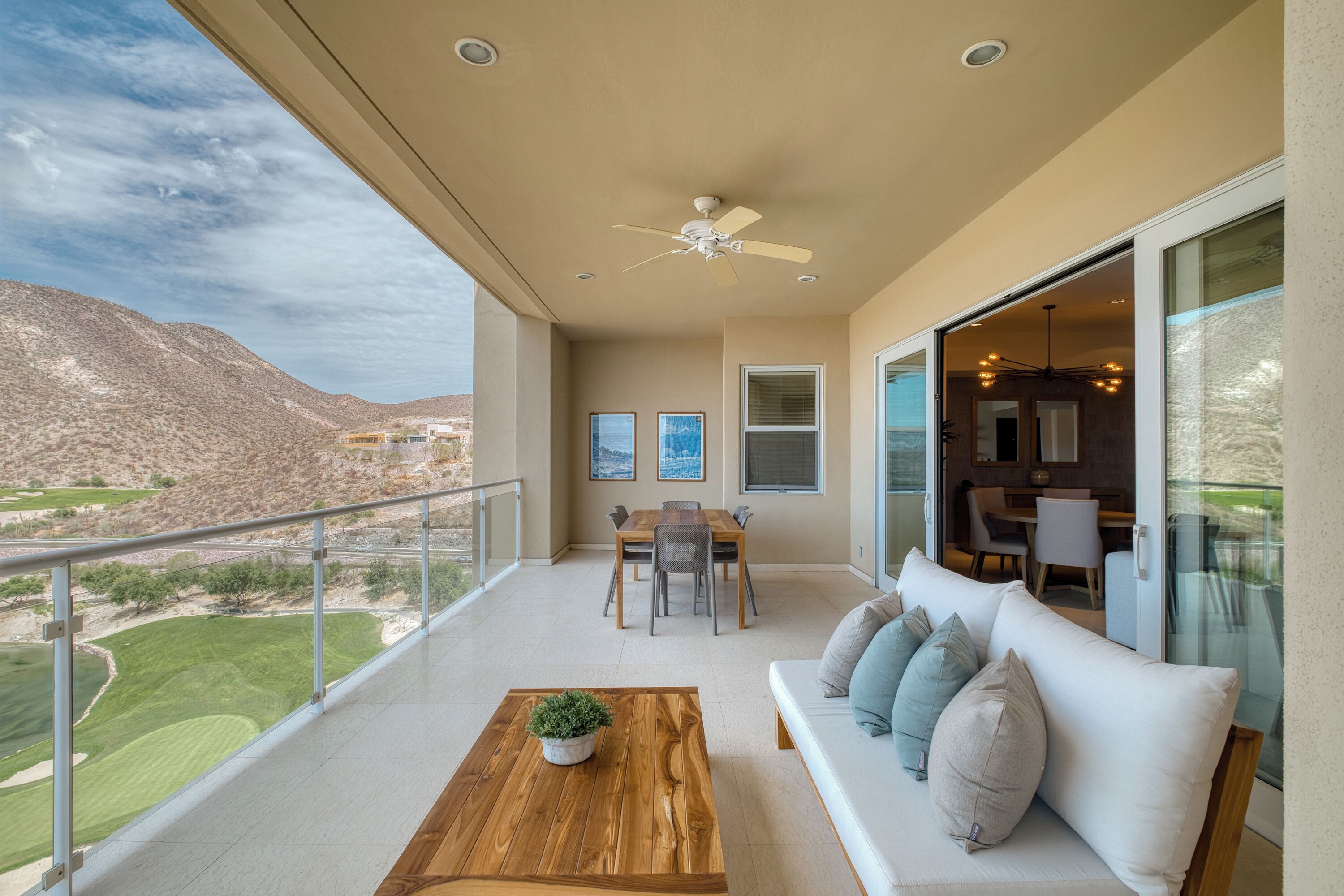 A spacious balcony with a wooden table, a sofa with cushions, and a dining area.