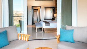 Habitación de hotel moderna con una cama grande, dos sofás, una mesa de centro de madera y vistas al desierto a través de amplios ventanales.