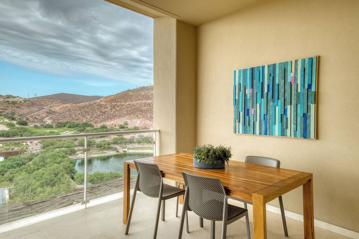 A dining area with a wooden table, two chairs, a potted plant, and a view of a river and mountains.
