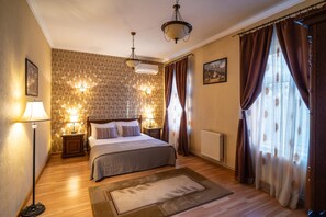 Habitación de hotel con cama, dos lámparas de noche, un radiador, una ventana con cortinas y una pared con estampado floral.