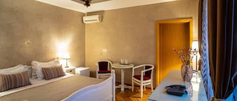 Habitación de hotel con cama, mesitas de noche, escritorio con teléfono, una silla, una pequeña mesa con un florero y un equipo de aire acondicionado.
