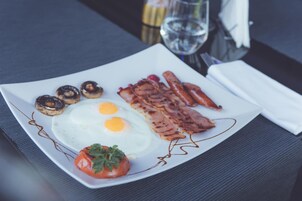 Un plato de desayuno con huevos, tocino, champiñones y tomate.