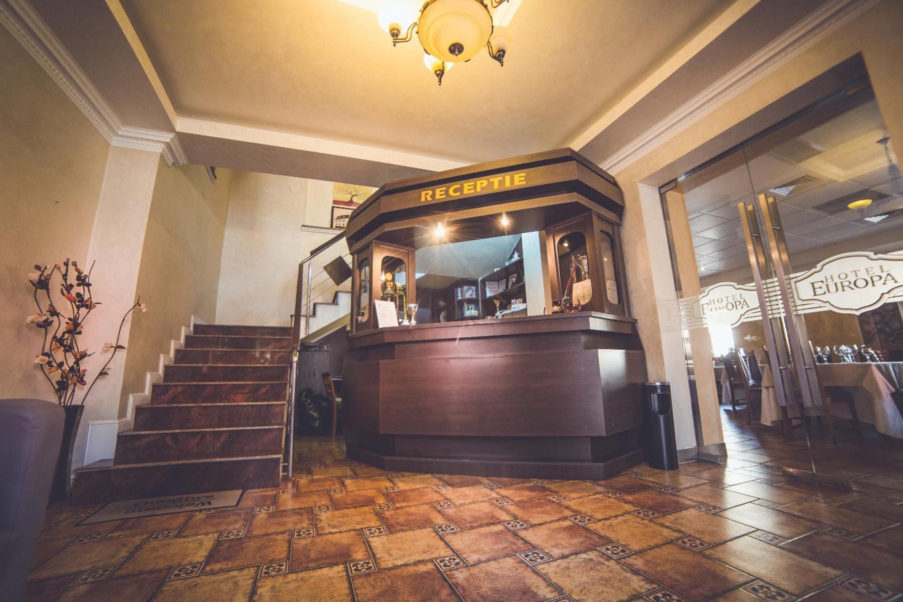 A reception area with a reception desk, a staircase, and a view of the hotel Europa.