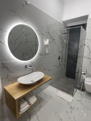A modern bathroom with a marble vanity, a round mirror, a shower enclosure, and a toilet.
