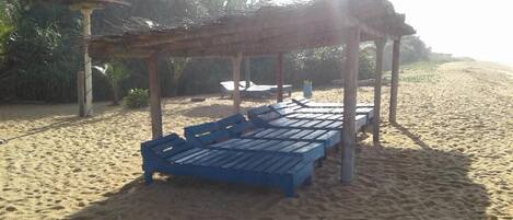 A beach with wooden lounge chairs and a thatched-roof structure.