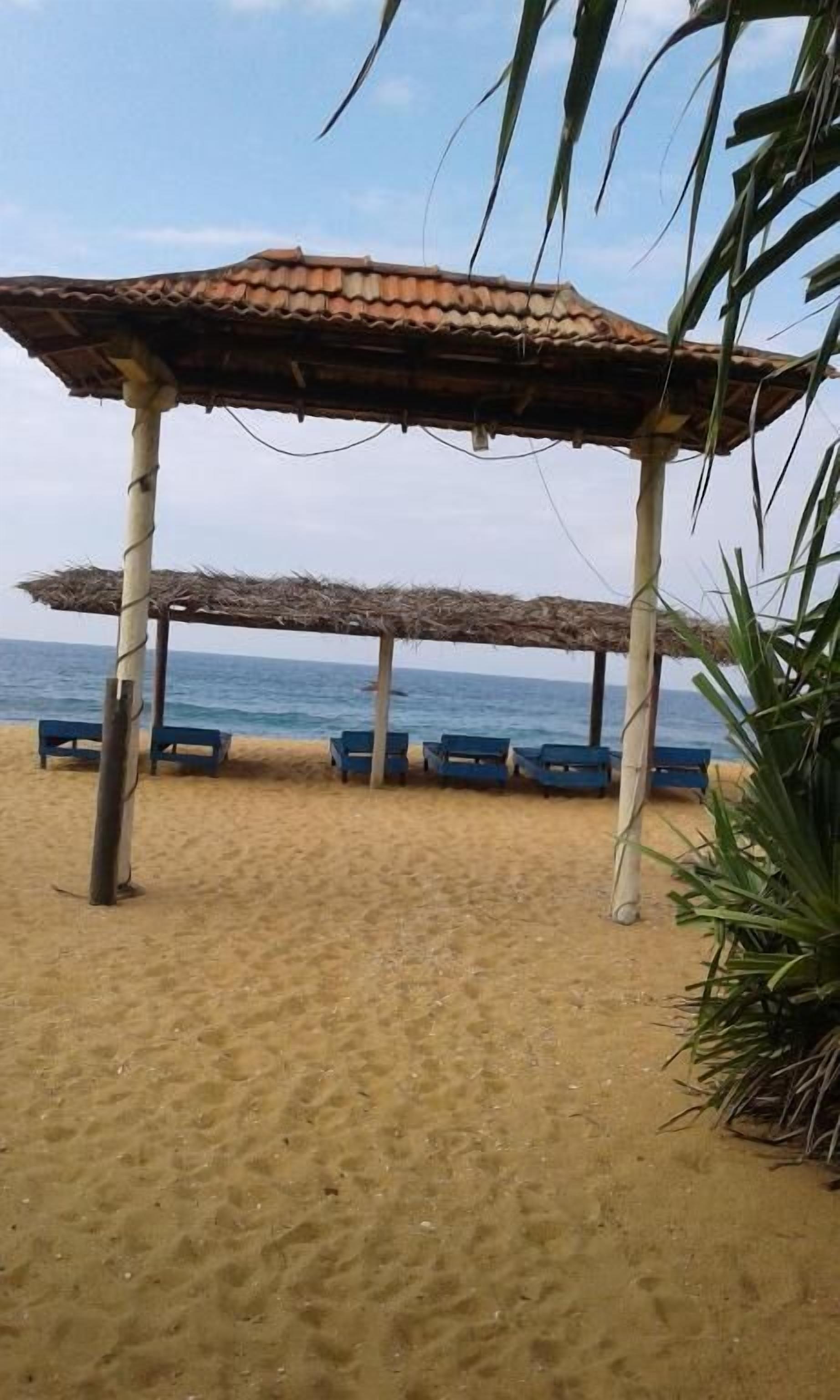 A beach with a thatched-roof gazebo and blue lounge chairs.