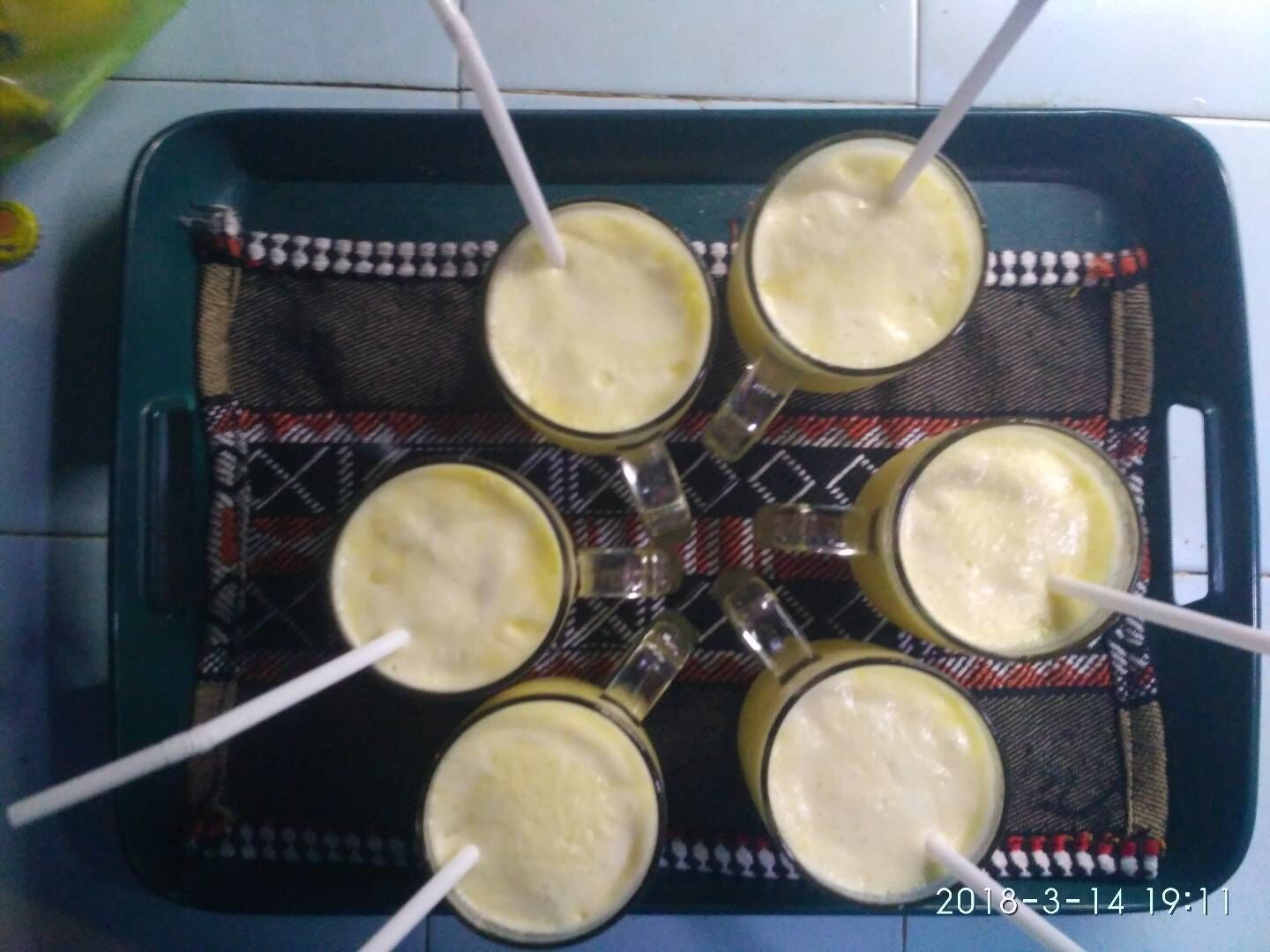 Un plateau contenant six verres remplis d’une boisson crémeuse, chacun muni d’une paille, posé sur une nappe à motifs.