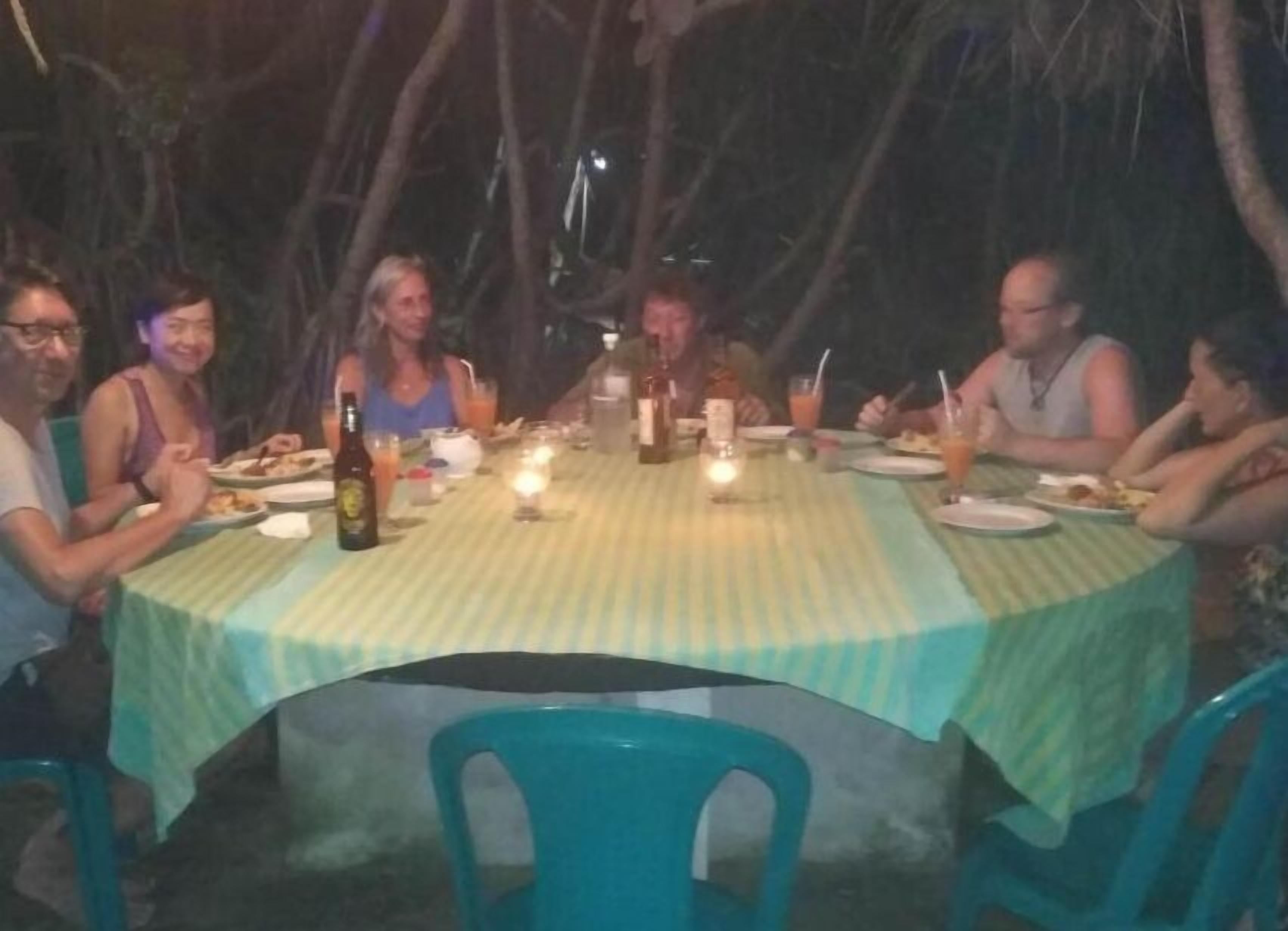 A group of people dining at an outdoor table with a green tablecloth, surrounded by trees.