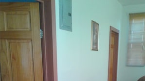 Una habitación con puerta de madera, un sofá marrón, un tapete pequeño y una ventana con persianas.
