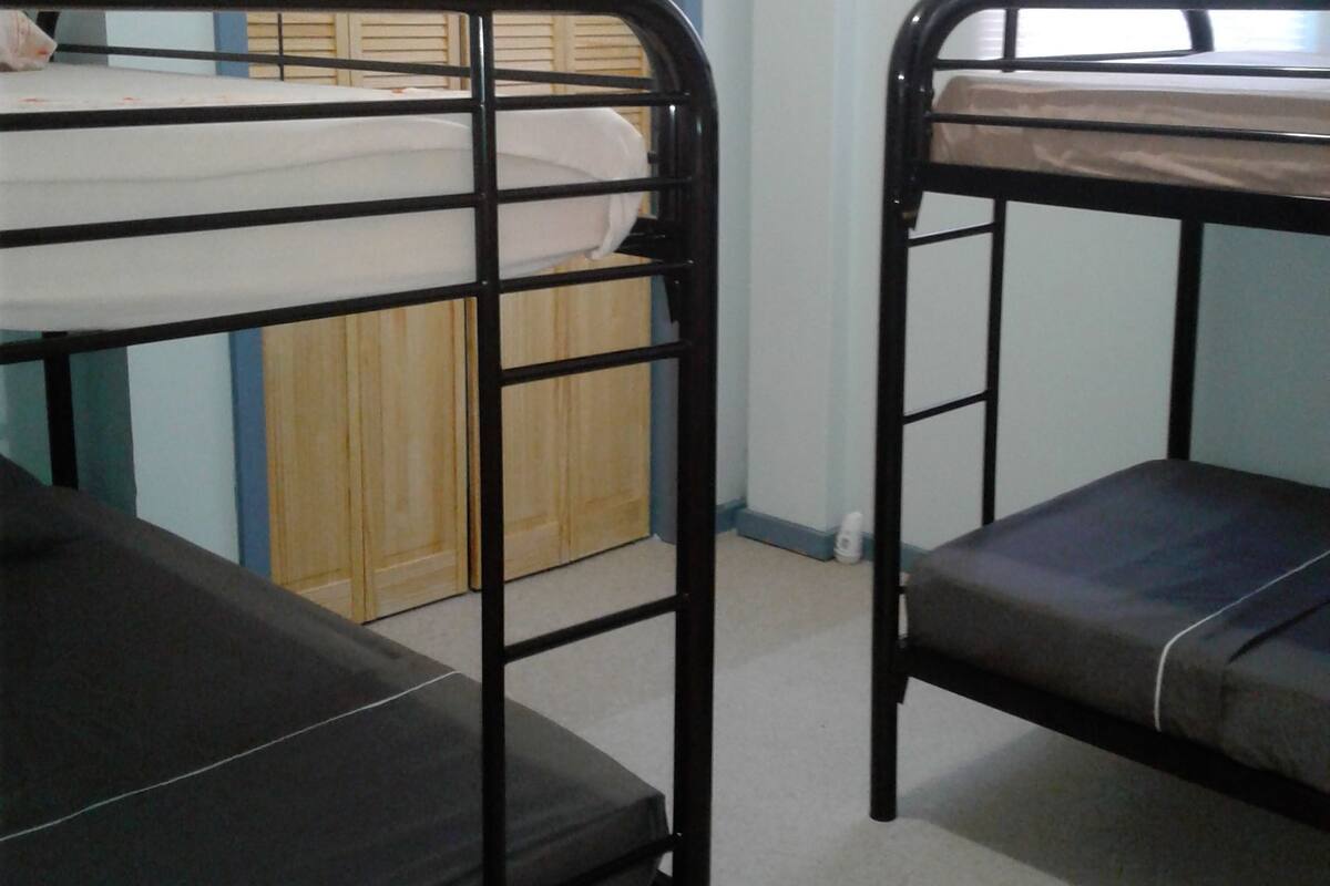 Two bunk beds in a room with a wooden wardrobe and a window with blinds.