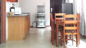 Cocina compacta con estufa, microondas y armarios. Zona de comedor con mesa y sillas.